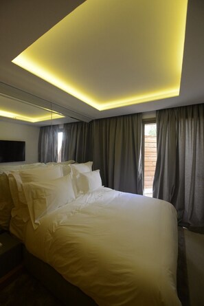 A hotel room with a large bed, a flat-screen TV mounted on the wall, and a window with curtains.