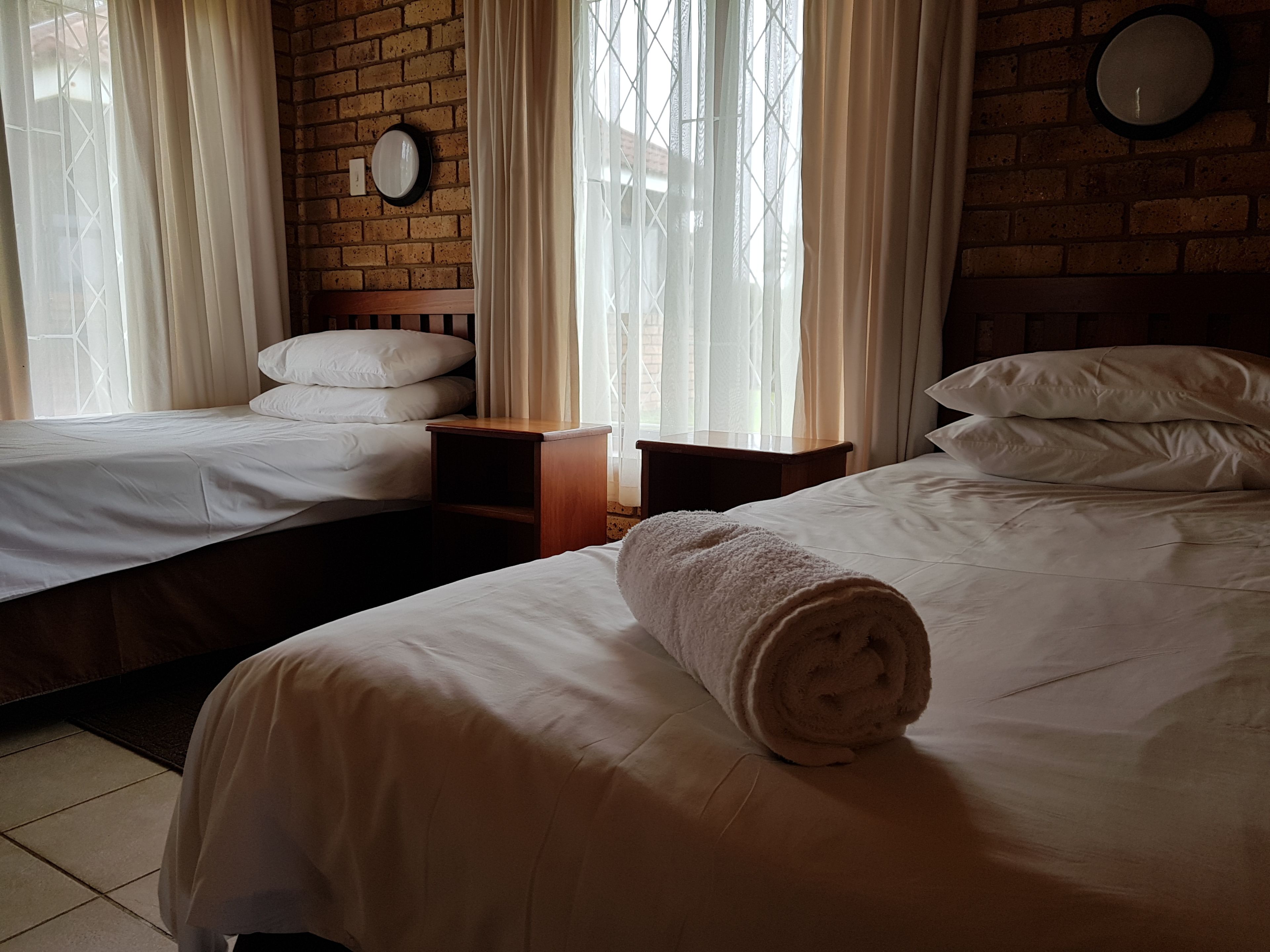 Una camera d'albergo con due letti, un muro in mattoni, una sveglia e tende leggere.