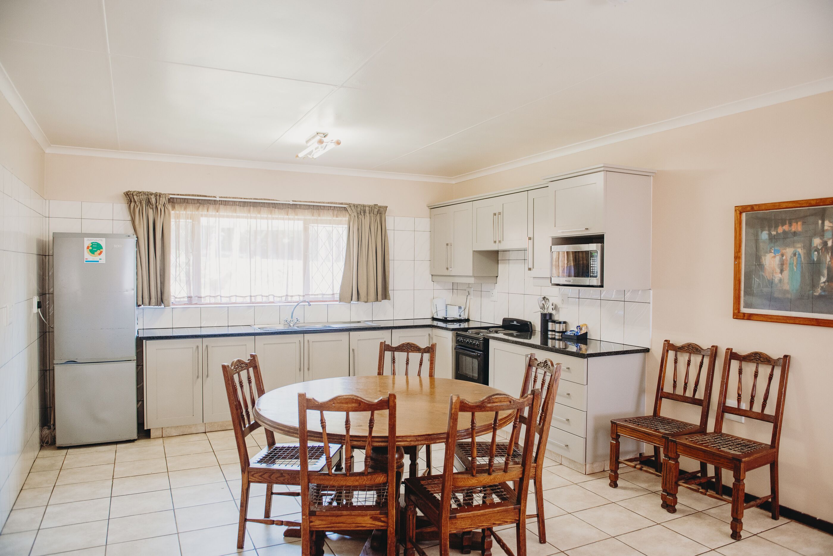 A compact kitchen with a dining area, white cabinets, a refrigerator, and a microwave.