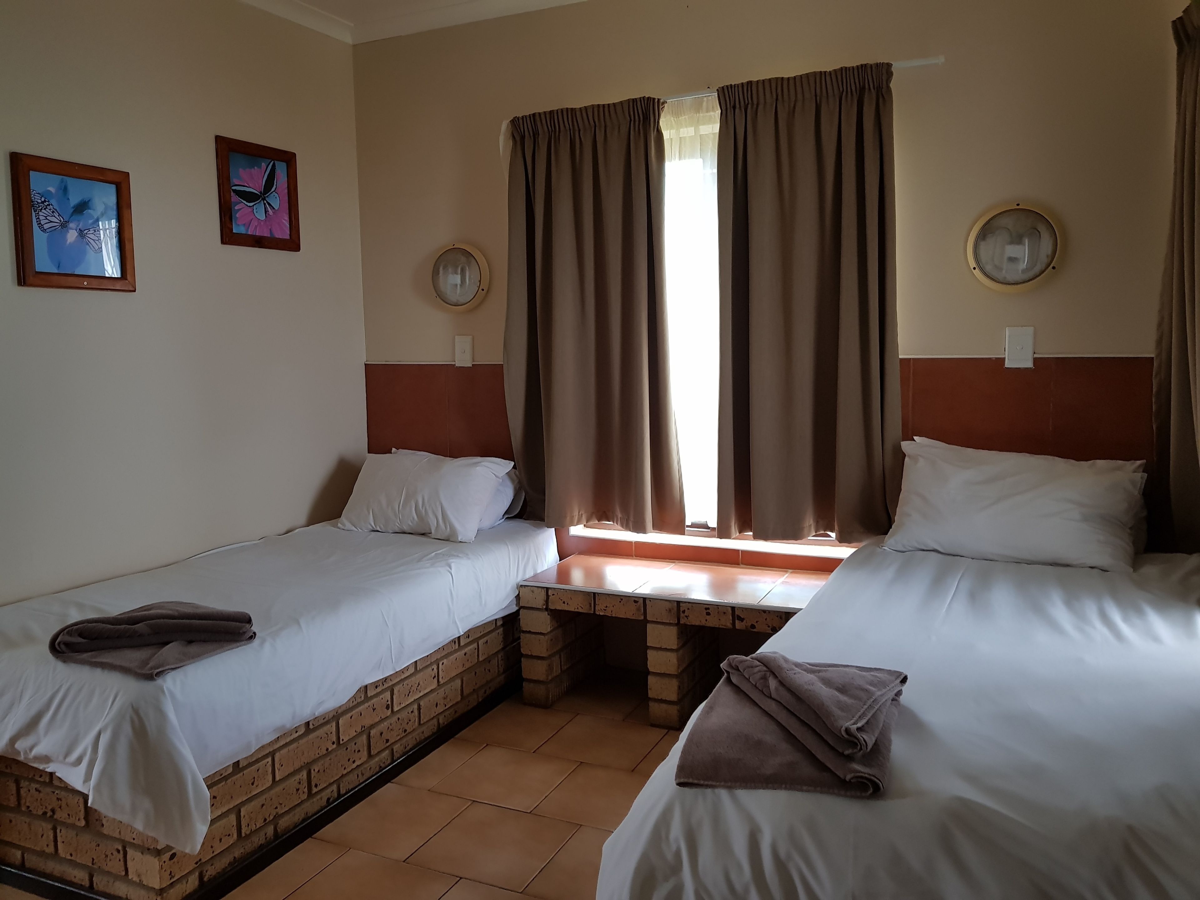 Une chambre avec deux lits, une cloison en briques et une fenêtre avec des rideaux.