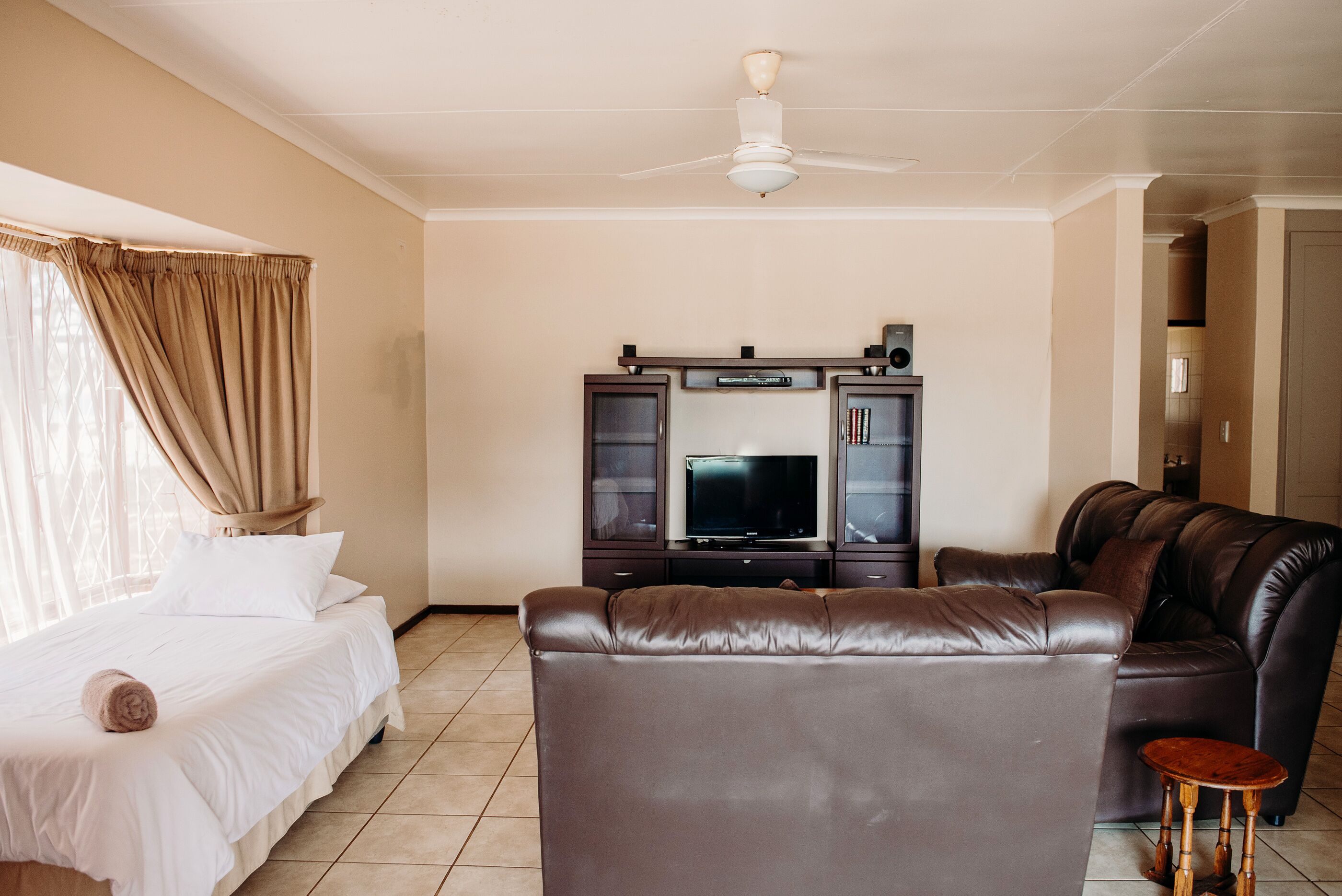 Quarto de hotel com cama, sofá de couro, televisão e ventoinha de teto.