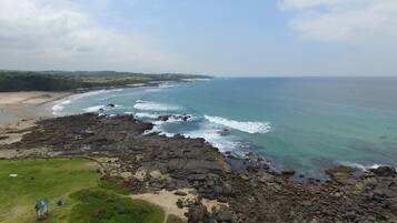 A coastal landscape with a rocky shoreline, a sandy beach, and a grassy area with a sign.