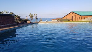 A swimming pool with a view of the sea, surrounded by buildings and palm trees. - Port Edward Holiday Resort (Port Edward)