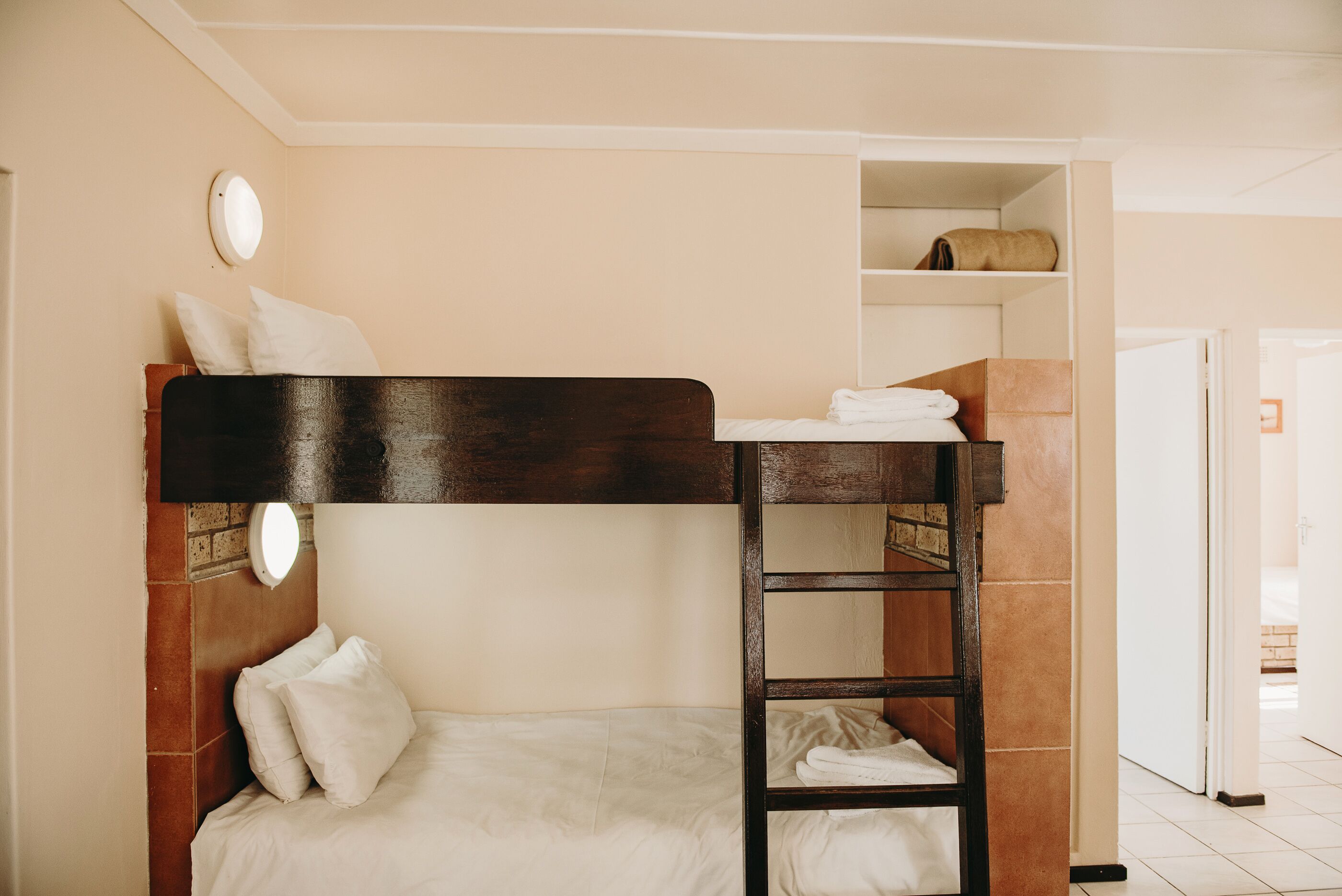 Un lit superposé avec une échelle, un oreiller blanc et une étagère avec des serviettes pliées.