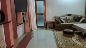 A living room with a sofa, a television, a patterned rug, and a door leading to another room. - Sarada Lodge Hotel (Ouagadougou)