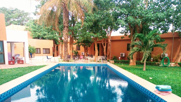 A swimming pool with a blue decorative border, surrounded by a grassy area and trees. - Sarada Lodge Hotel (Ouagadougou)