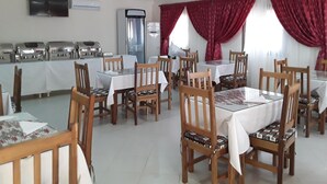 A dining area with multiple tables and chairs, a buffet line, and a ceiling fan. - Sarada Lodge Hotel (Ouagadougou)