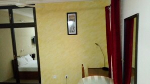 A hotel room with a bed, a chair, a desk, a mirror, and an air conditioning unit. - Sarada Lodge Hotel (Ouagadougou)