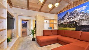 A modern living room with a large sectional sofa, wooden shelving, a flat-screen TV, and a mountain landscape mural on the wall. - Residence Treyer (Terento)