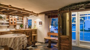 A cozy room with a wooden bar, a dining table, and a bench. There is a window with a view of the outside. - Residence Treyer (Terento)