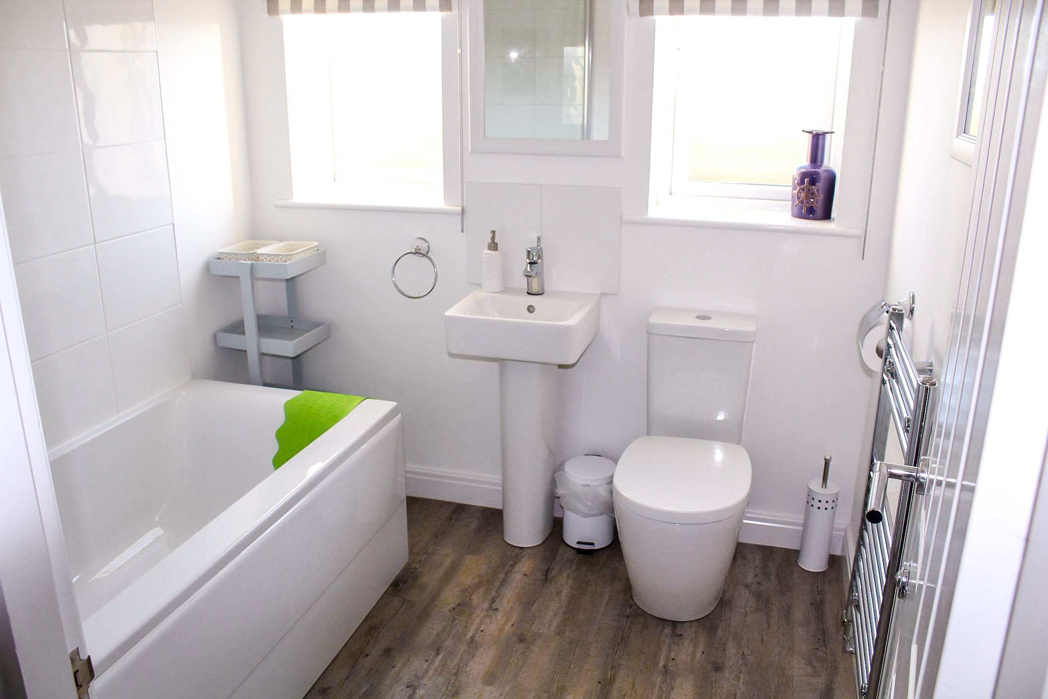 A bathroom with a bathtub, sink, toilet, and a window with a vase.