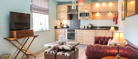 A modern living room with a flat-screen TV, a sofa, a coffee table, and a dining area with a microwave and oven.