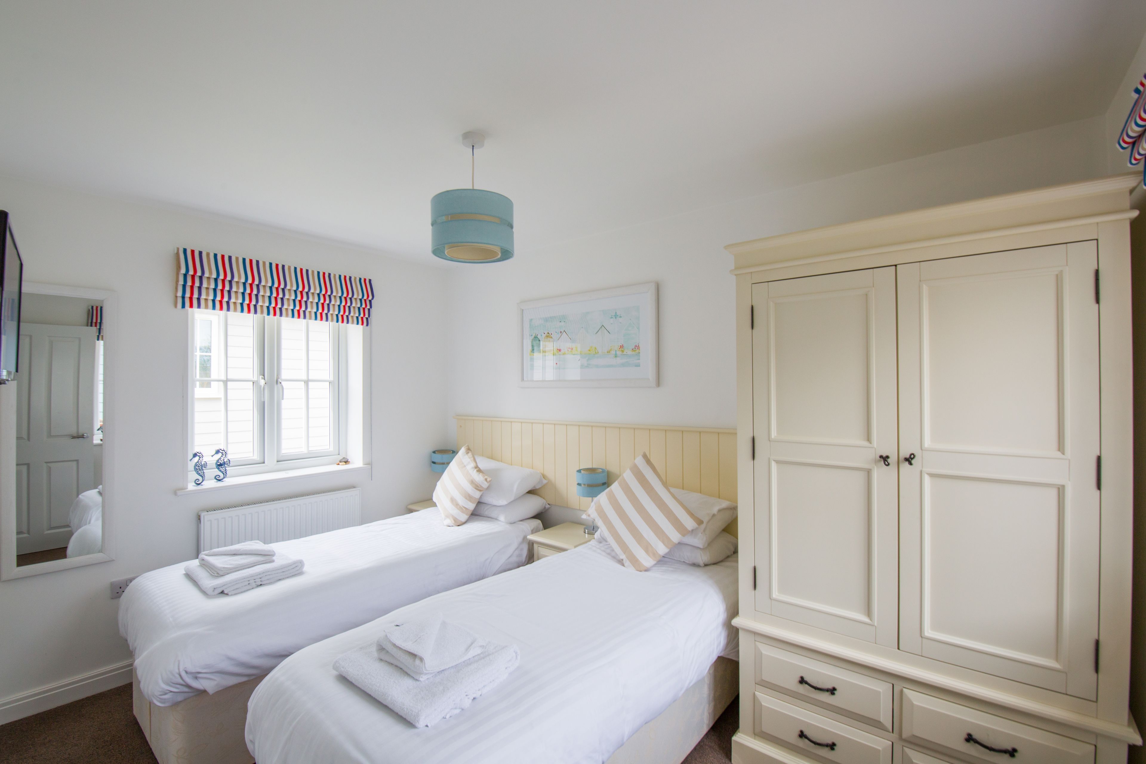 Une chambre avec deux lits, une armoire, une fenêtre avec des rideaux, un radiateur et un tableau accroché au mur.