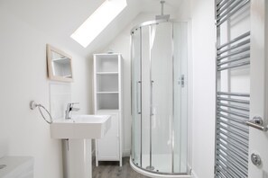 A modern bathroom with a glass shower enclosure, a white sink, and a built-in shelf.