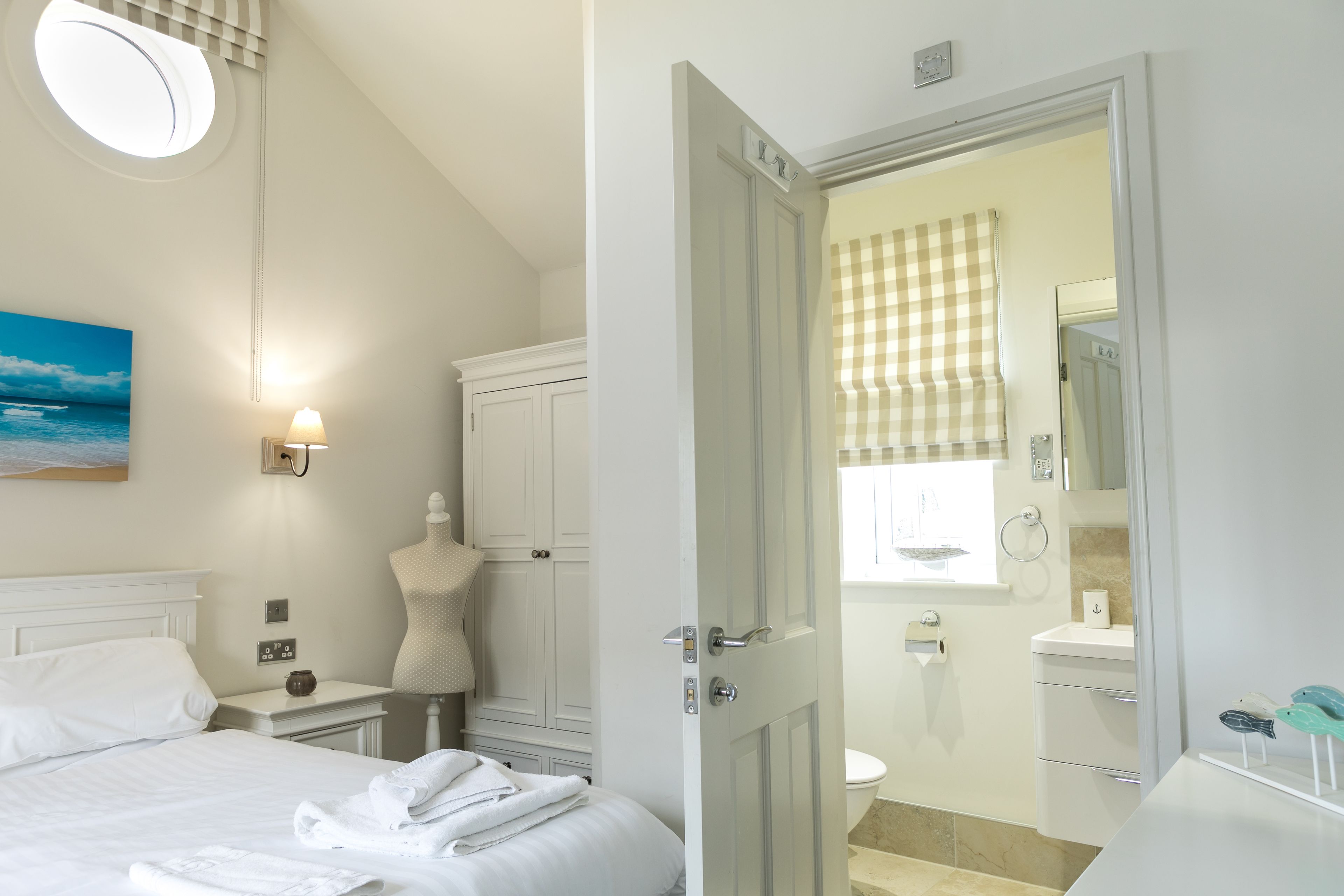 Habitación de hotel con cama, mesita de noche, lámpara, cómoda y baño visible a través de una puerta abierta.
