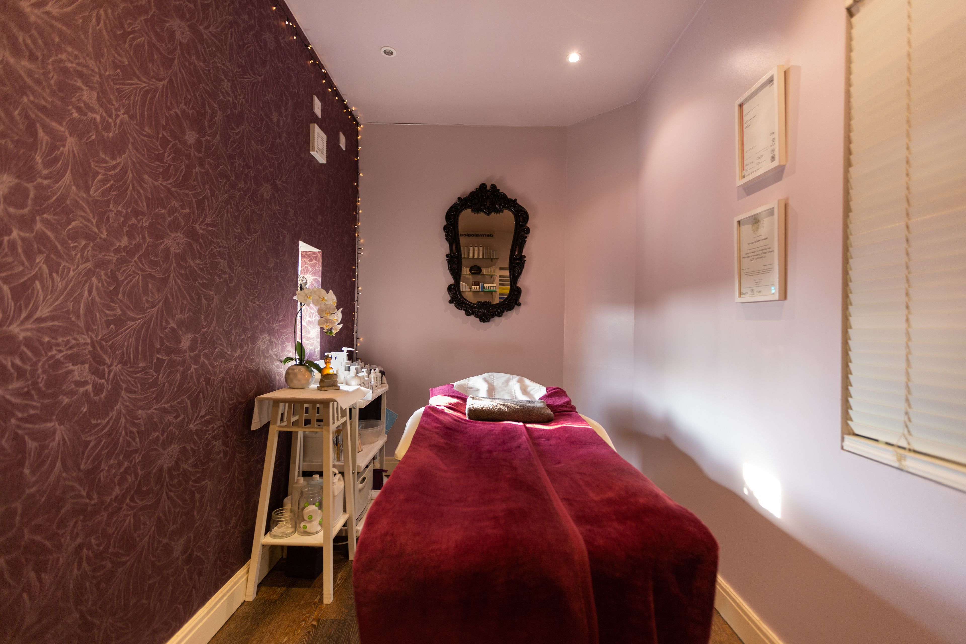 A room with a bed covered in a red blanket, a vanity with toiletries, and a mirror on the wall.