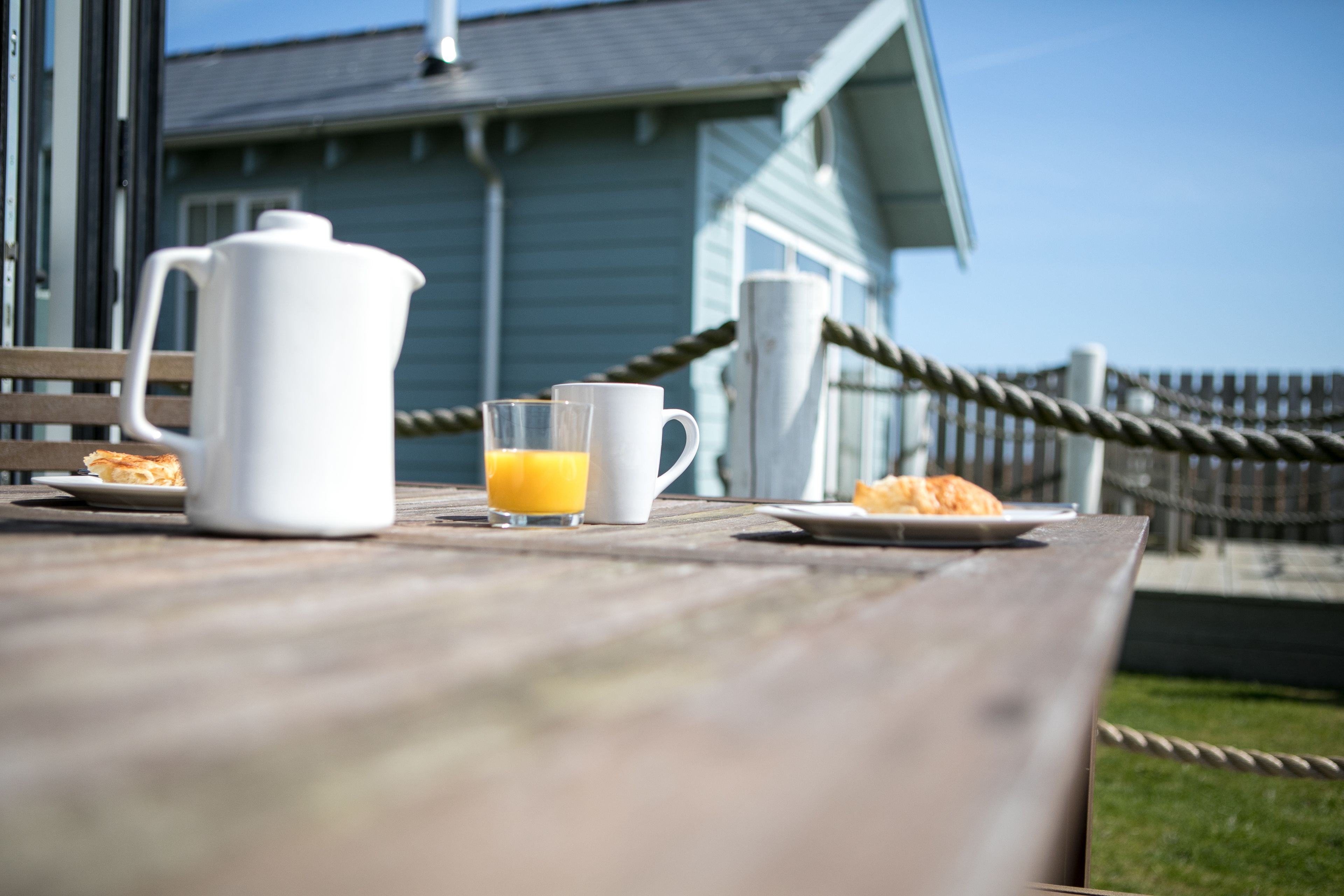 A wooden table with a white pitcher, a glass of orange juice, and a plate of food.