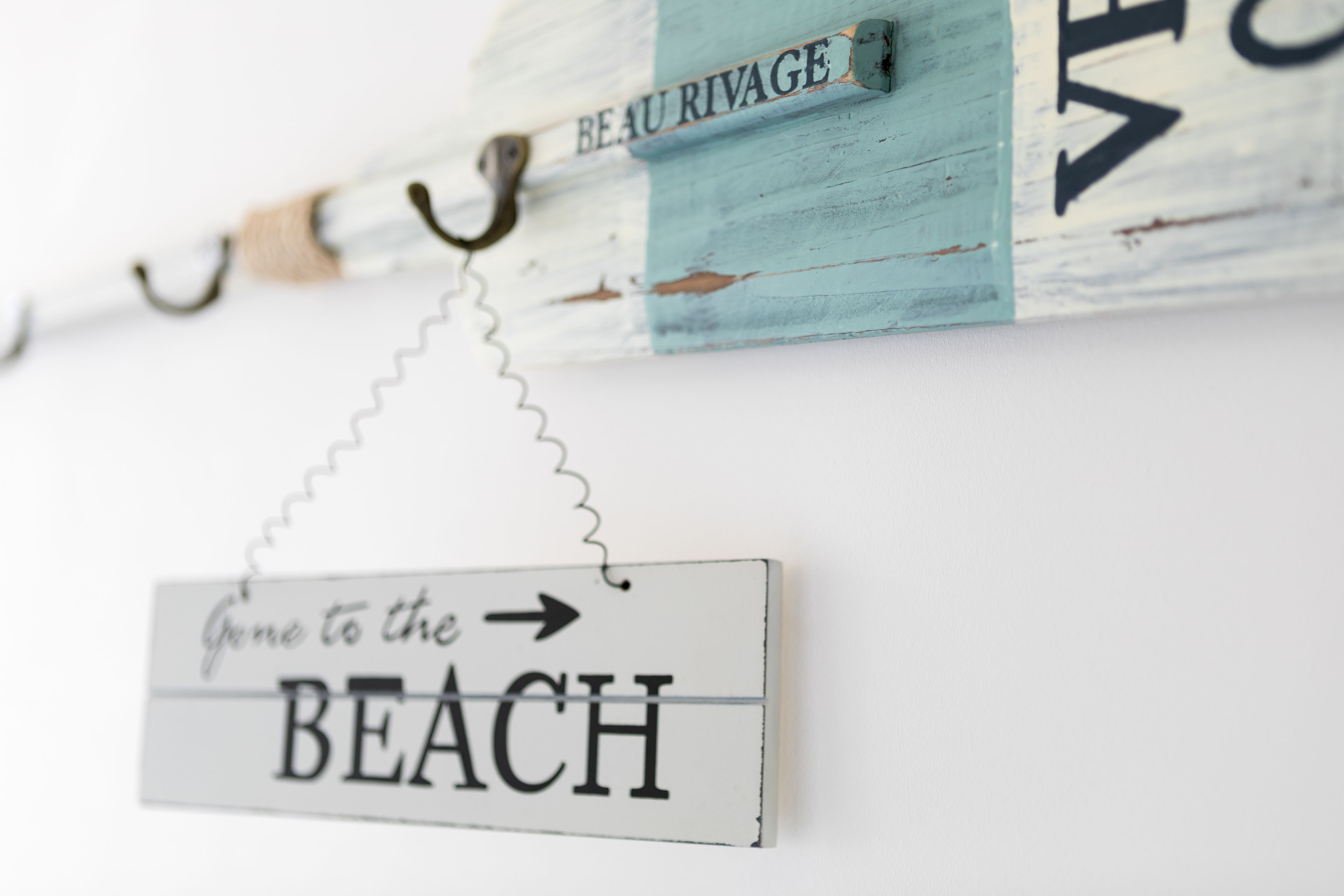 A rustic sign with the words "BEACH" and "BEAU RIVAGE" on a wall.
