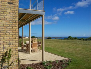 A patio with outdoor furniture, a stone wall, and a view of the sea.