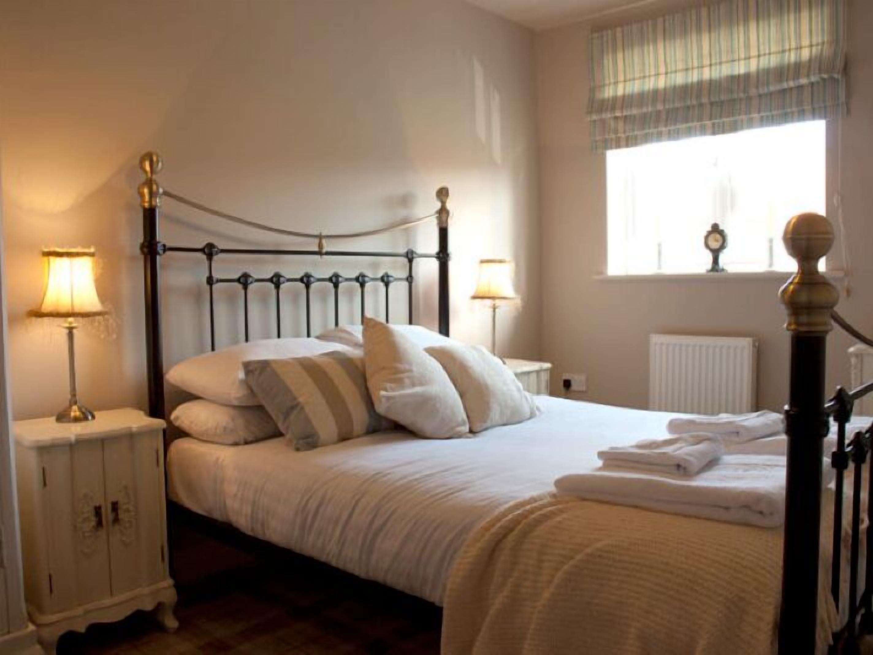 A neatly made bed with pillows, a bedside table with a lamp, and a window with curtains.