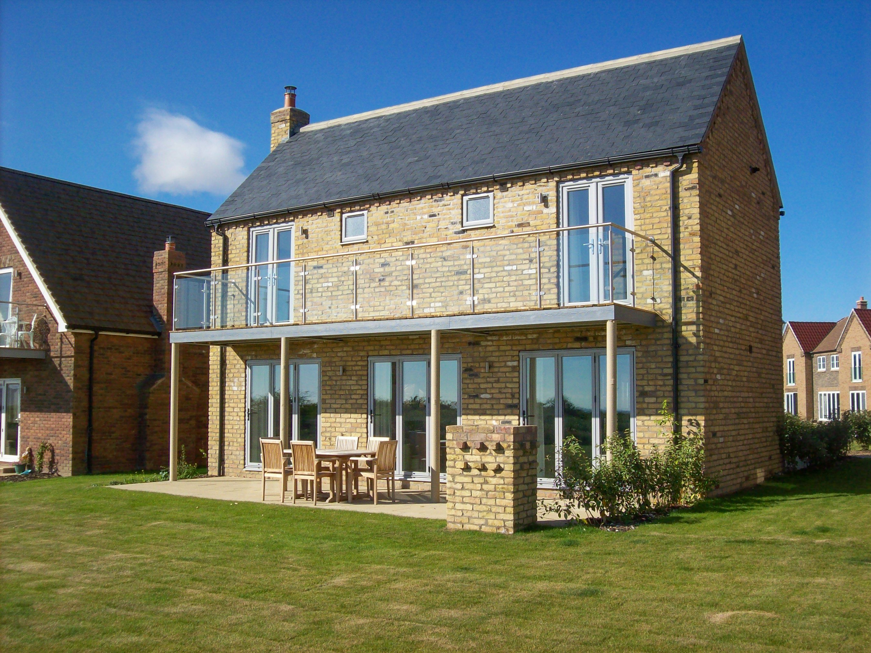 A two-story house with a balcony, large windows, and a patio area with outdoor furniture.