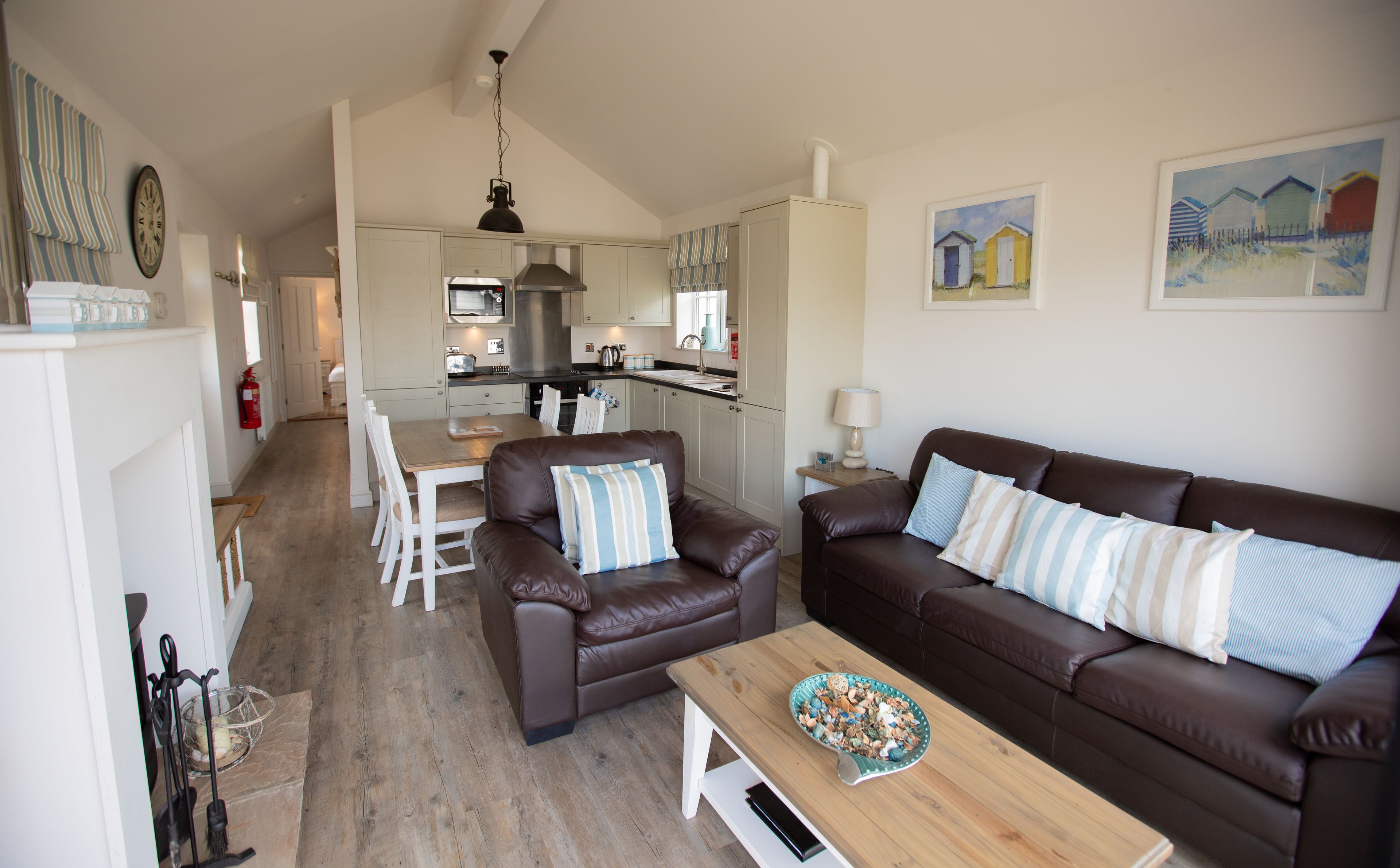 A cozy living room with a brown leather sofa, a wooden coffee table, and a dining area with white chairs.