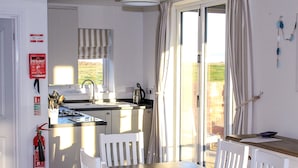 A kitchen with a gas stove, sink, and white cabinets. There is a fire extinguisher on the wall and a window with curtains.