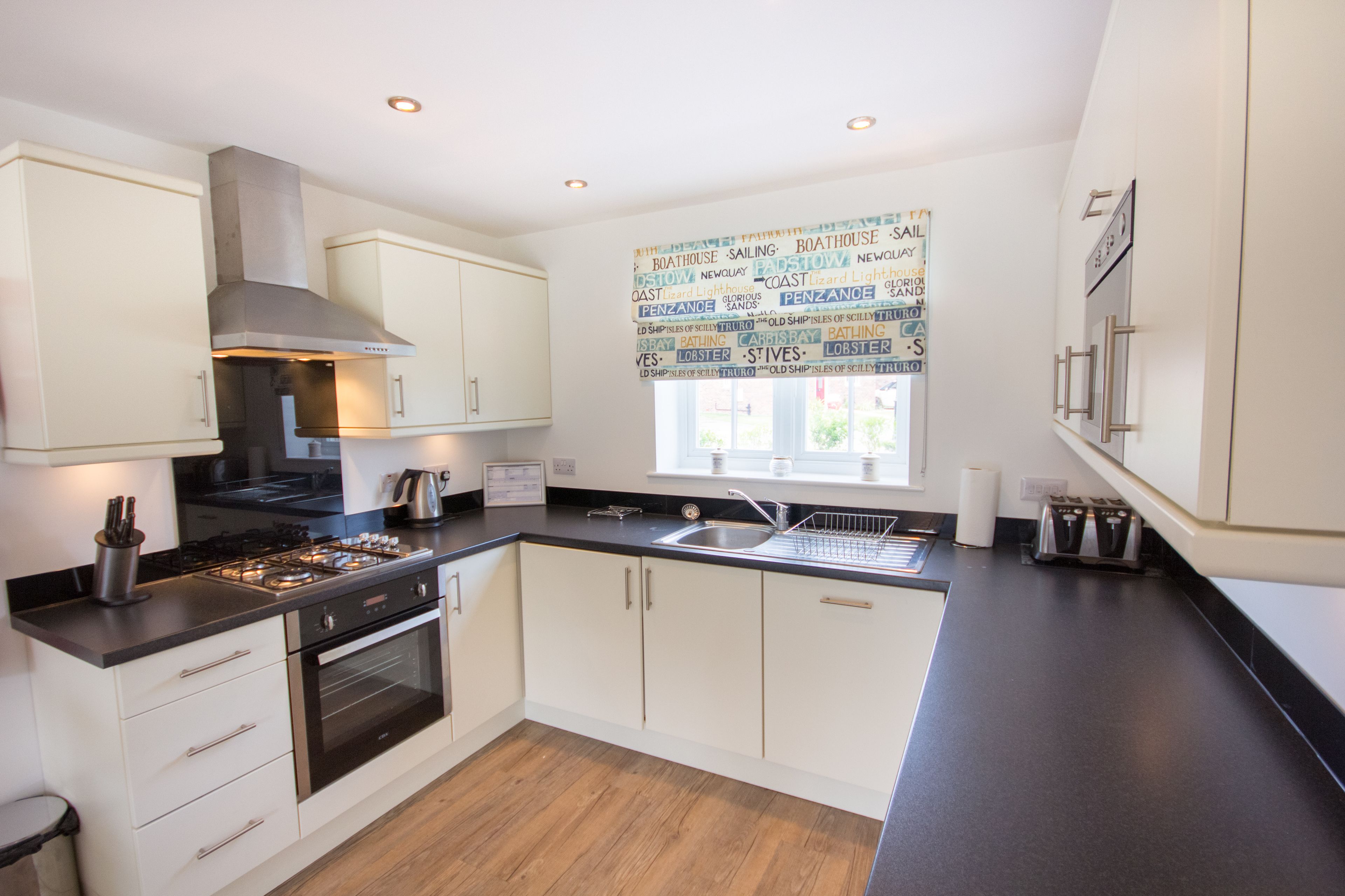 A modern kitchen with white cabinets, a black countertop, stainless steel appliances, and a window with a nautical-themed view.