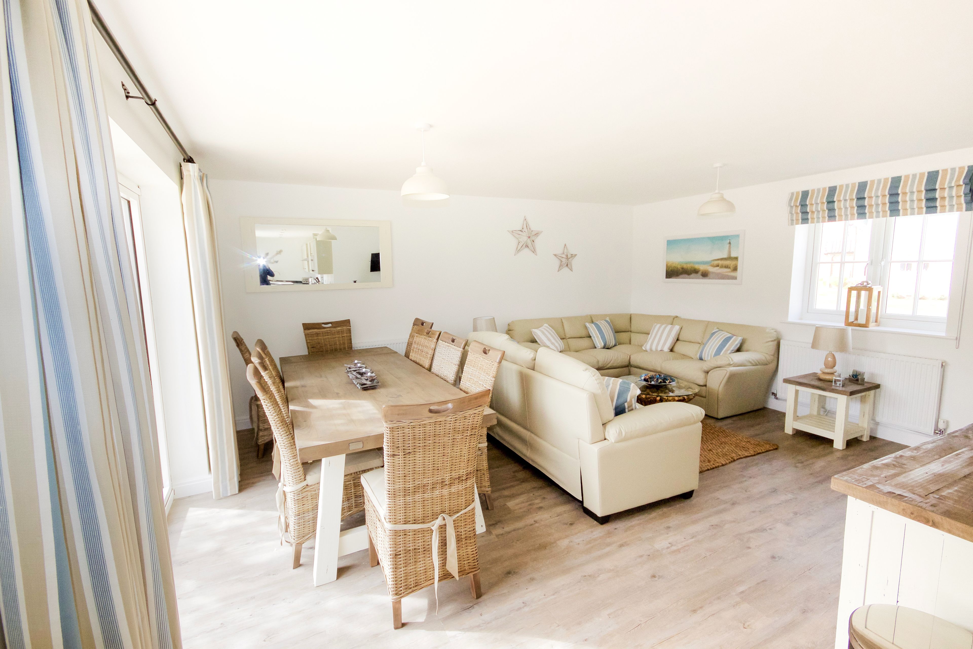 A spacious living room with a large beige sofa, a dining table with wicker chairs, and a small side table with a lamp.