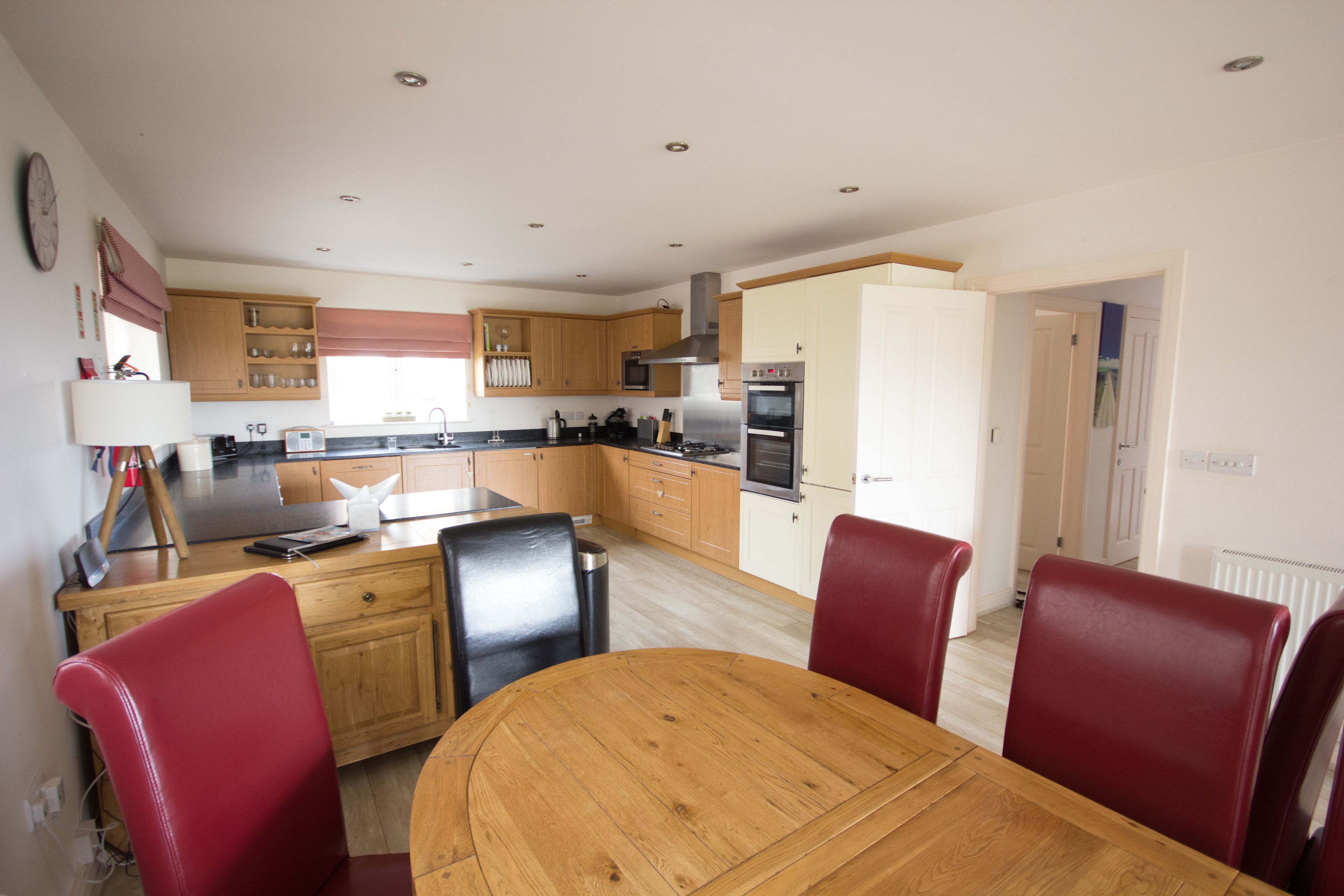 A modern kitchen with wooden cabinets, a central island, and red chairs around a wooden table.