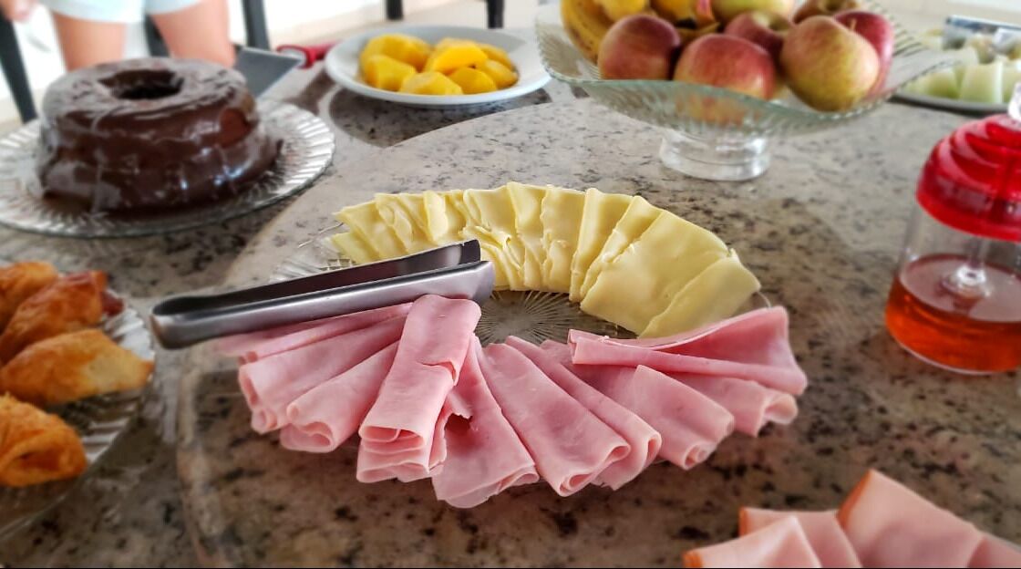 A table with various food items including a chocolate-covered donut, sliced yellow fruit, and pink sliced meat.