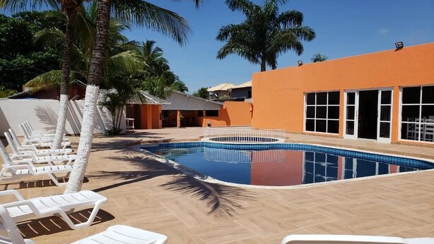 Zona de piscina con sillones de descanso, una pileta y palmeras.
