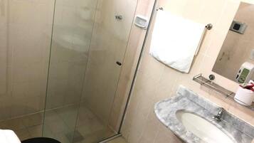 A bathroom with a glass-enclosed shower, a marble sink, and a white towel hanging on the wall.