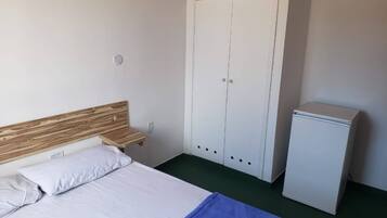 A bedroom with a bed, a wardrobe, and a small refrigerator.