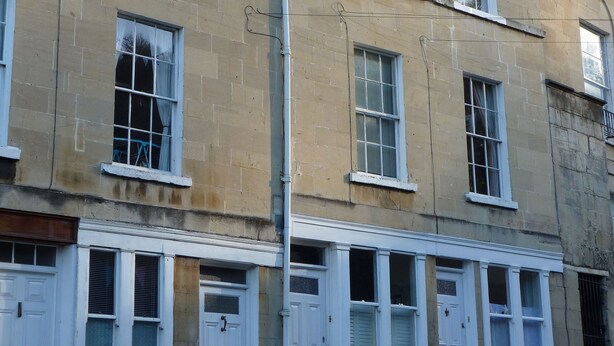 A multi-story building with a row of white-framed windows and doors, a visible chimney, and a street lamp. - Grade II listed terraced house in Bath, Somerset (Bath)