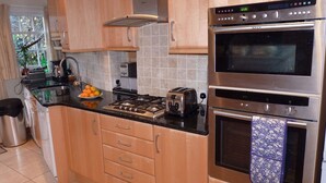 A modern kitchen with wooden cabinets, stainless steel appliances, a gas stove, a toaster, and a microwave. - Grade II listed terraced house in Bath, Somerset (Bath)