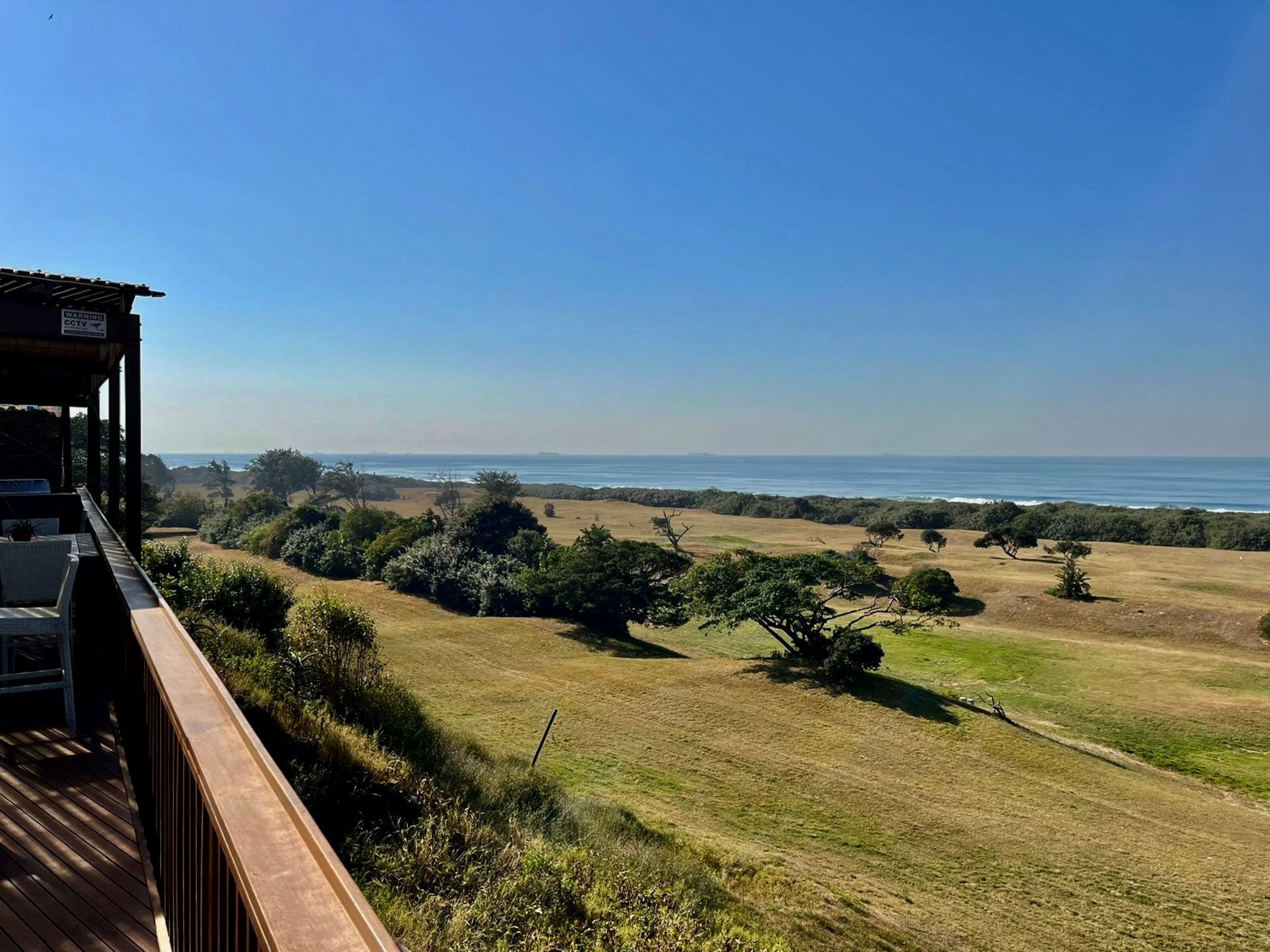 Vista de uma varanda com vista para uma paisagem gramada com árvores e uma praia.
