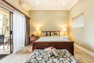 Un dormitorio con cama, lámparas de noche, mesita de noche, ventana con persianas y vistas a un espacio exterior.