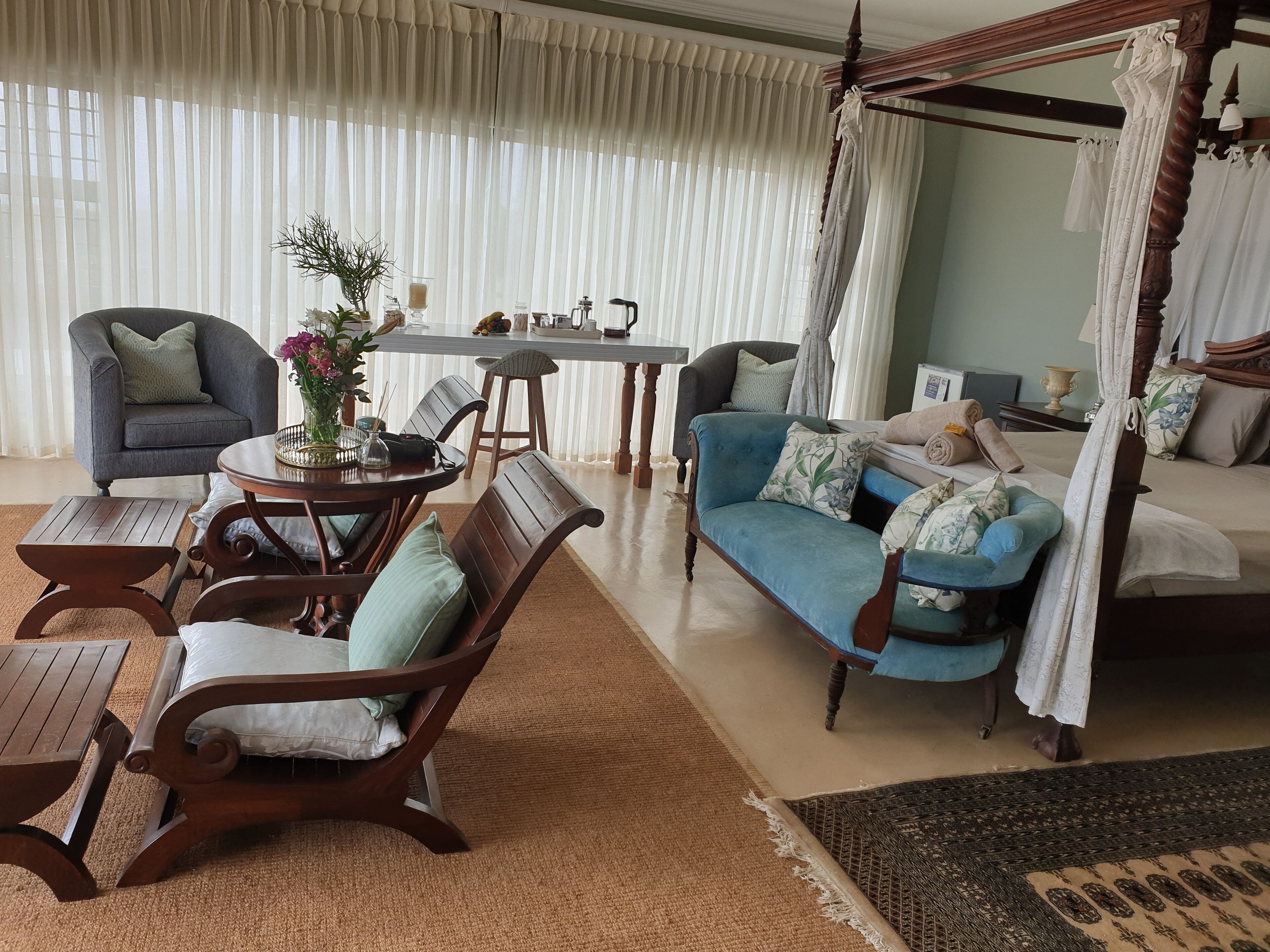 Un salon spacieux avec un lit à baldaquin, un canapé bleu et un coin repas comprenant une table et des chaises.