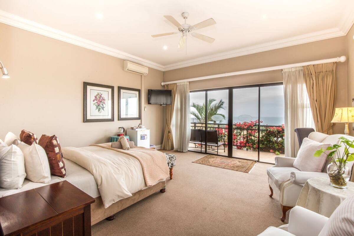 A hotel room with a bed, a desk, a chair, a TV, and a balcony with a view.