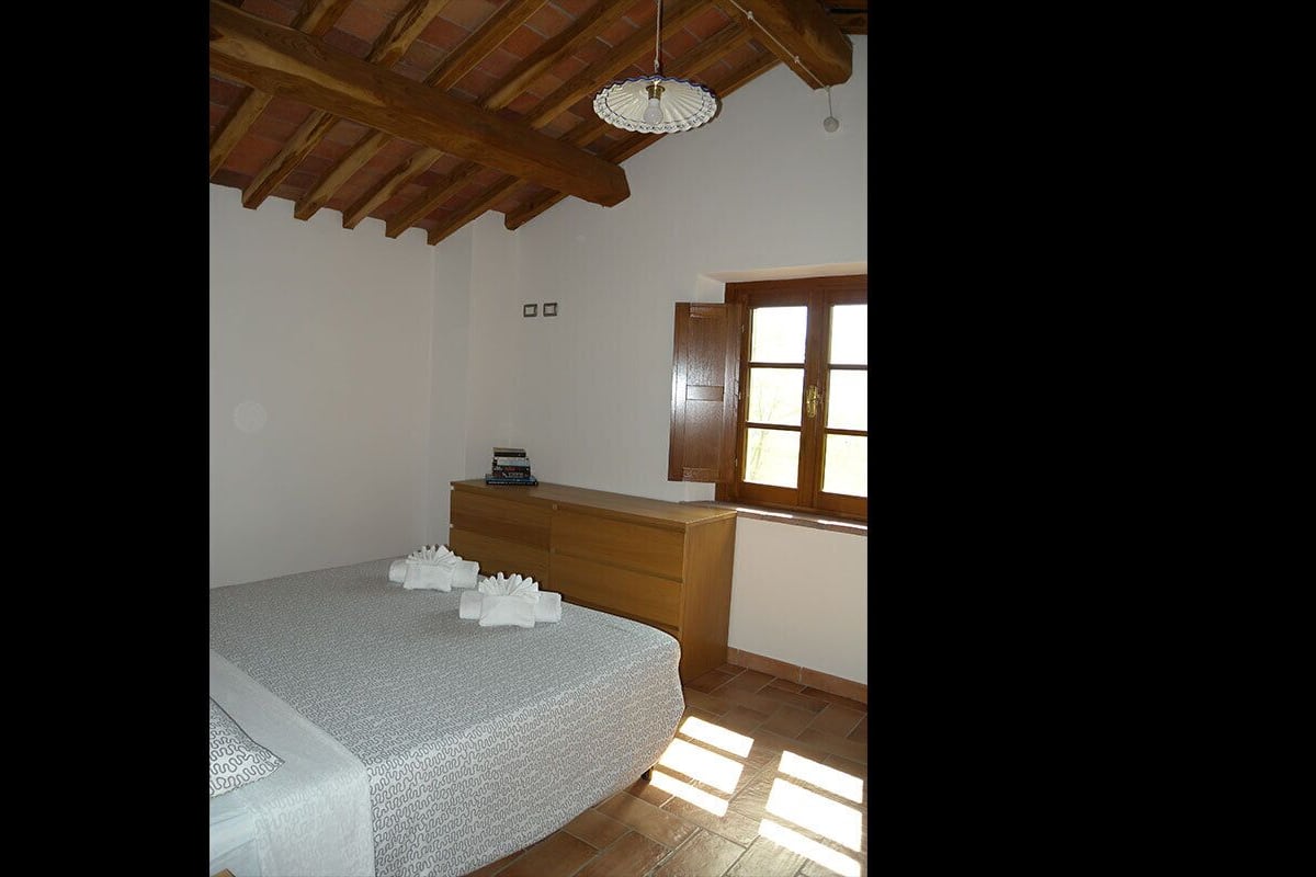 Een slaapkamer met een bed, een houten dressoir en een raam.