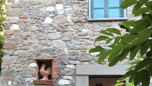 A stone building with a rustic exterior, a wooden table and chairs outside, and a metal fence.