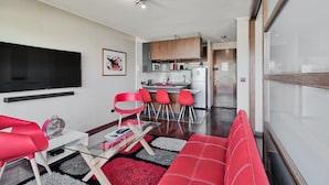 A modern living room with a flat-screen TV, red chairs, a glass coffee table, and a red sofa. - Red Velvet  Apartment (Santiago)