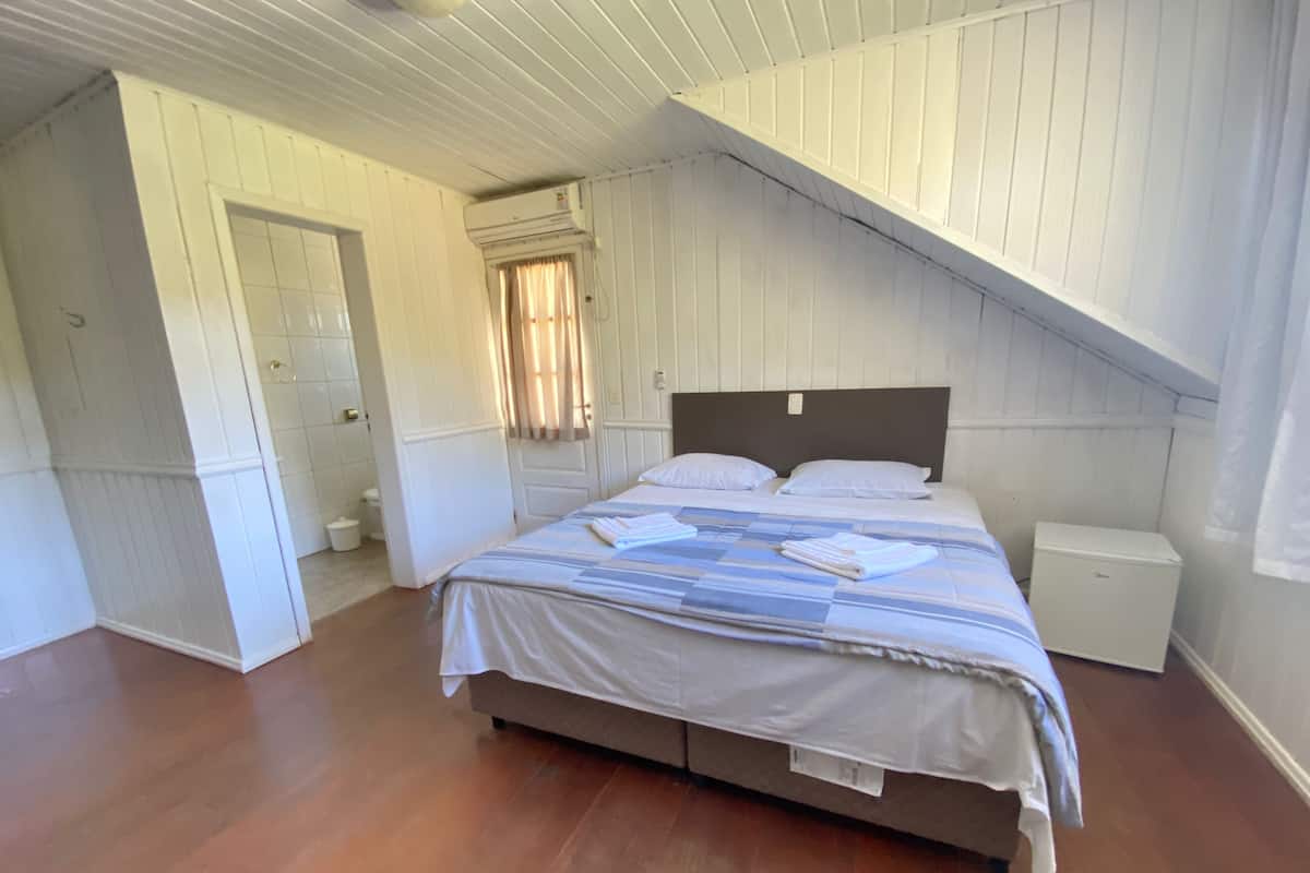Een slaapkamer met een groot bed, een nachtkastje, een klein wit kastje en een plafondventilator.