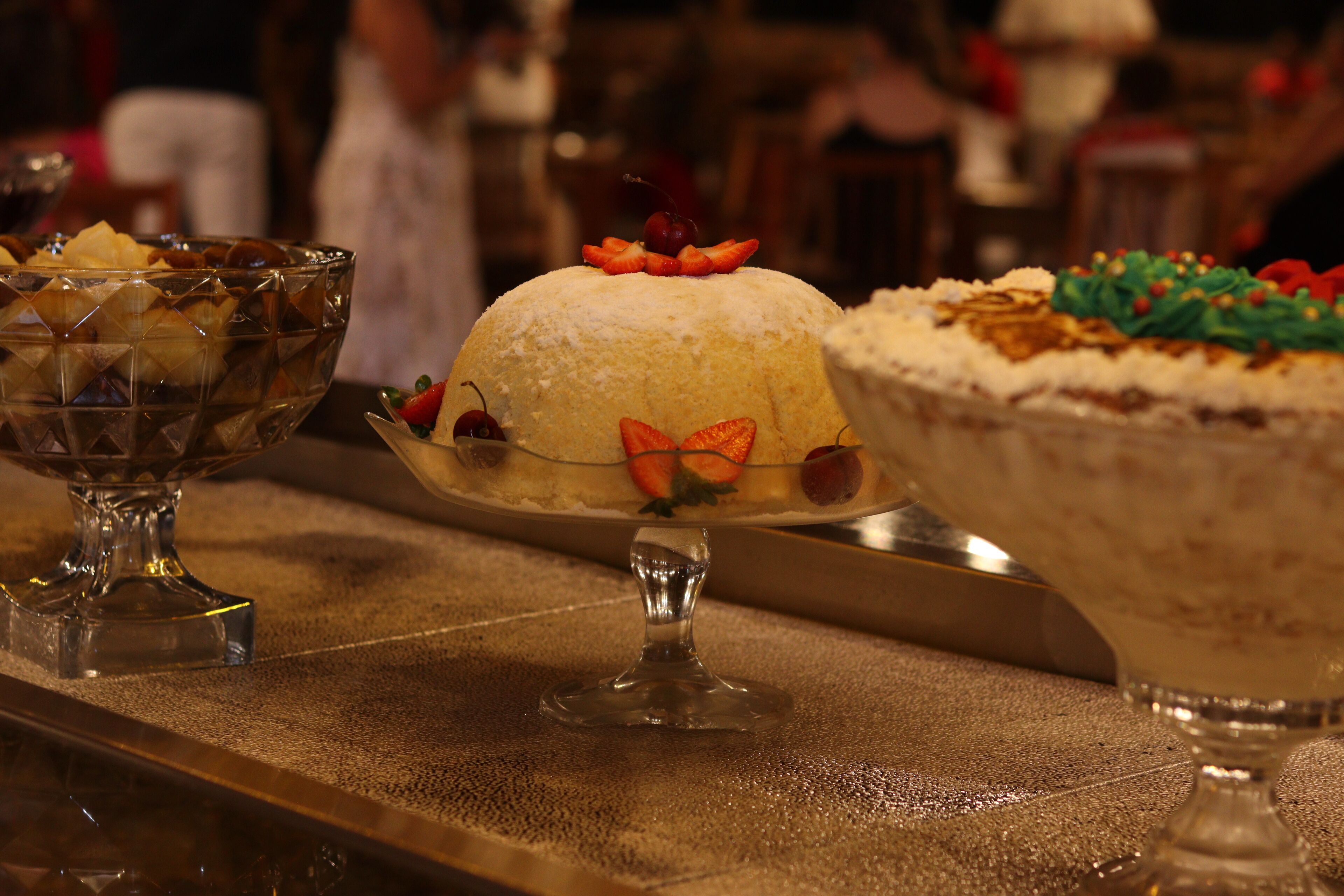 A dessert display with various cakes and a glass bowl containing fruit.