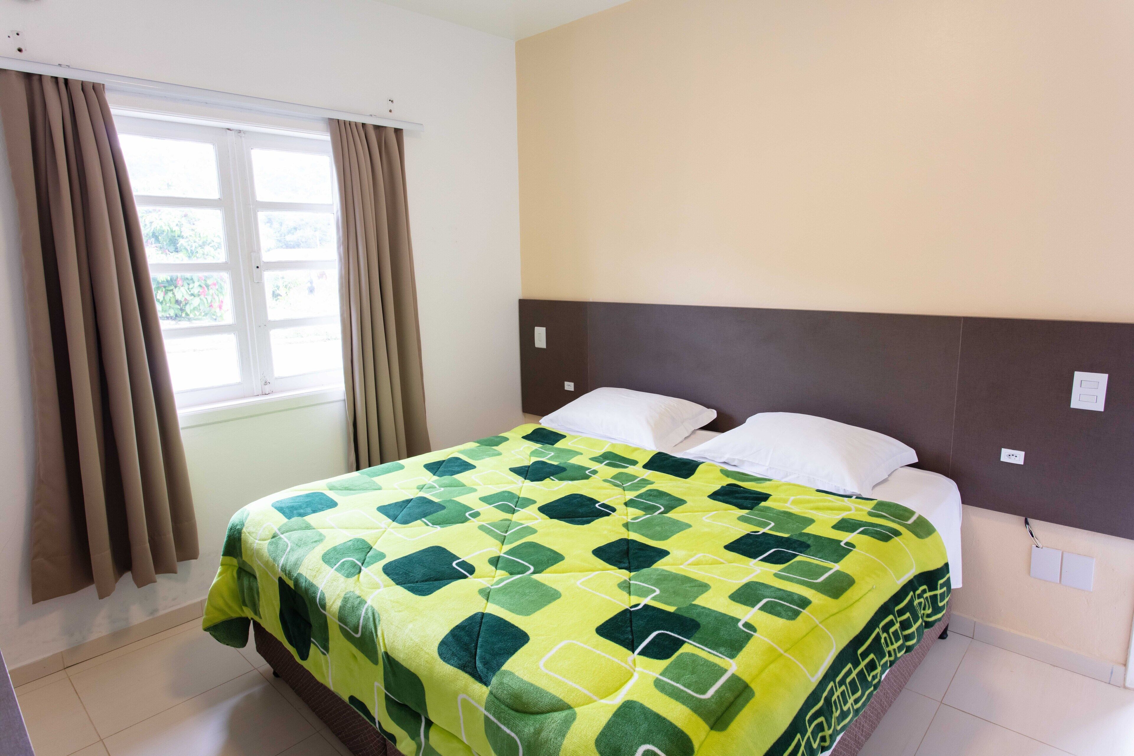 Una habitación de hotel con una cama, cortinas, una ventana y una pared con un interruptor de luz.
