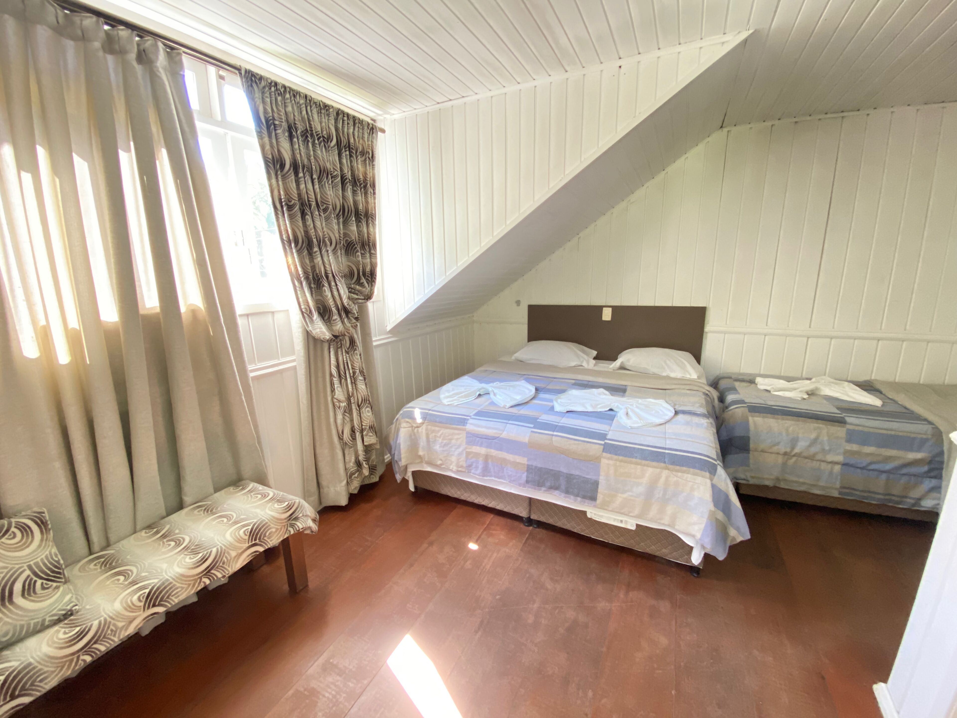 Una habitación con dos camas, un banco y una ventana con cortinas.