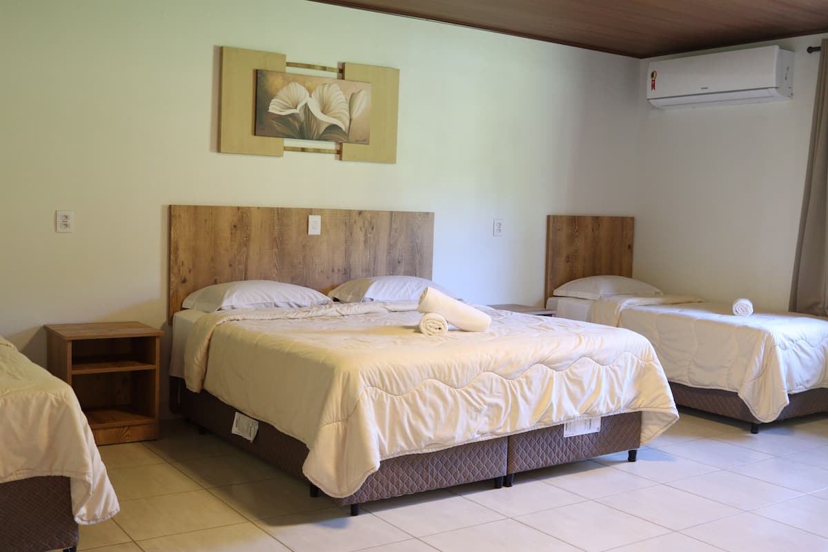 Een hotelkamer met een groot bed, twee kleinere bedden, een houten hoofdbord, een nachtkastje en een schilderij aan de muur.