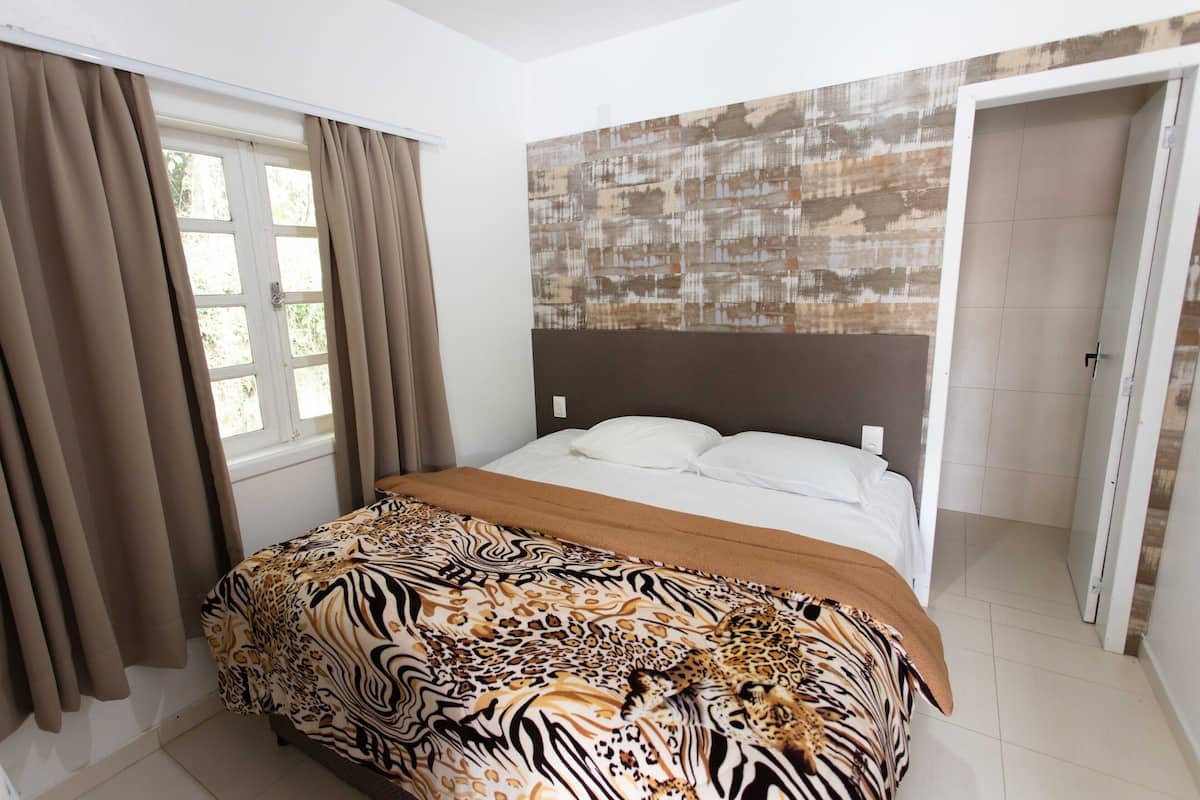 Een slaapkamer met een bed, gordijnen, een hoofdbord met een patroon en een deur.
