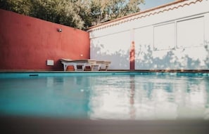 A swimming pool with a red wall and a white building in the background.